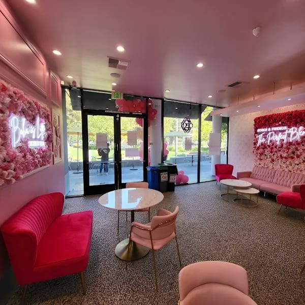Pink and red velvet seating, flower walls with neon signs, and glass tables in a cafe.