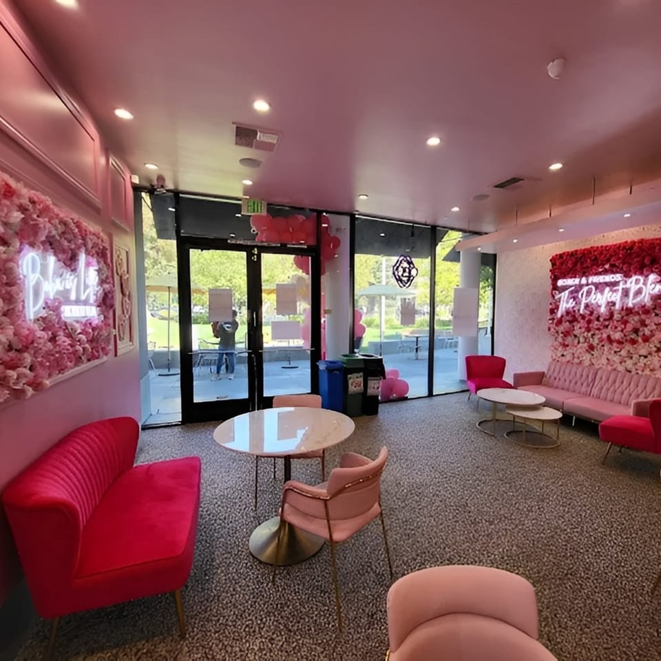 Pink and red velvet seating, flower walls with neon signs, and glass tables in a cafe.