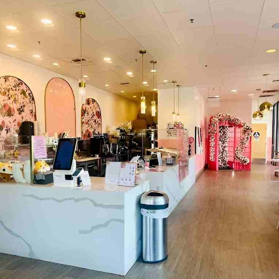 Modern cafe interior with a white marble counter, pink arched wall decor, and a floral phone booth.