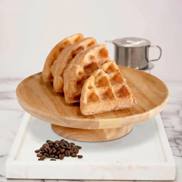 Four triangular waffles on a wooden stand, with coffee beans and a metal coffee filter nearby.