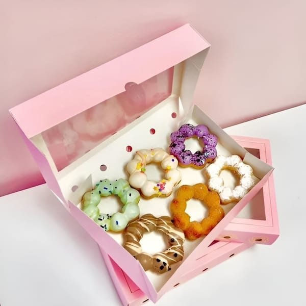 Six colorful mochi donuts with various glazes and sprinkles in a pink box.
