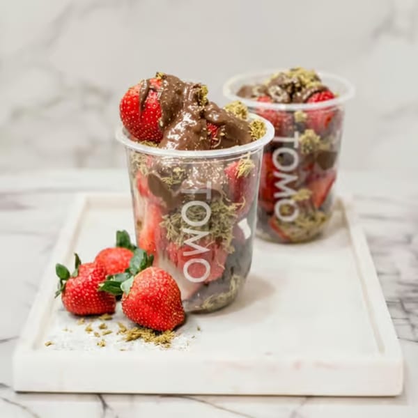 Two clear cups of strawberries with chocolate and green powder, plus loose strawberries on a white tray.