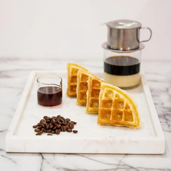 Waffles, coffee beans, syrup, and a Vietnamese phin coffee maker on a marble tray.