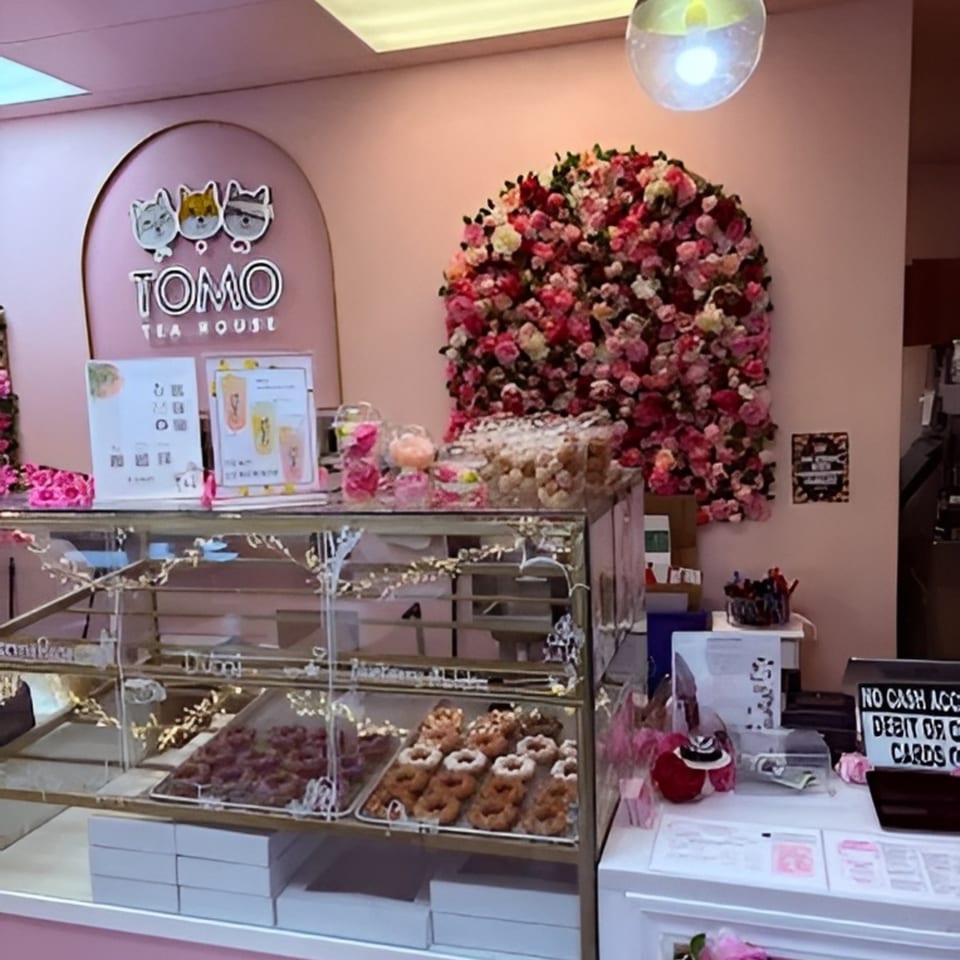 Interior of Tomo Tea House with a donut display case, pink walls, and a large floral arrangement.