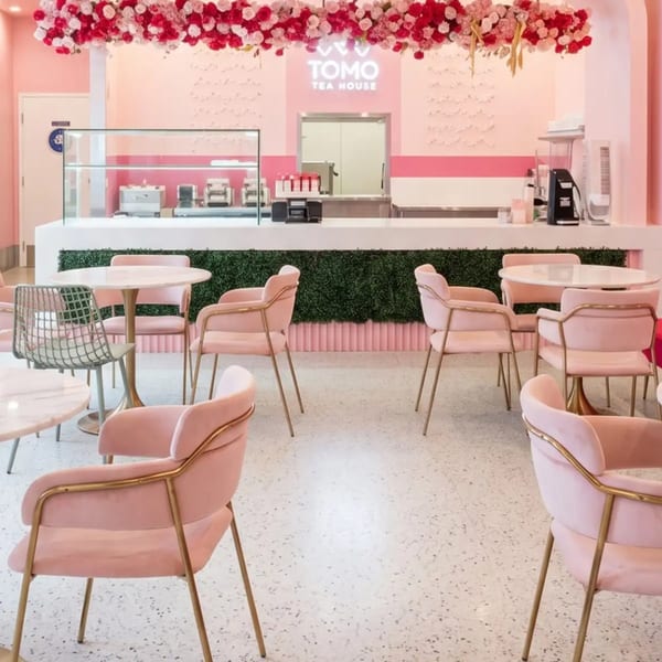 Pink-themed Tomo Tea House interior with pink chairs, white tables, and a floral ceiling decoration.