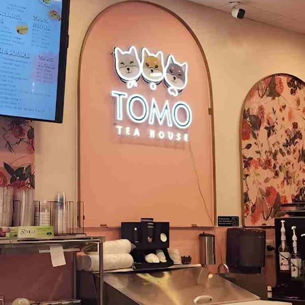 Tomo Tea House interior with a neon sign featuring three cat faces and the restaurant name.